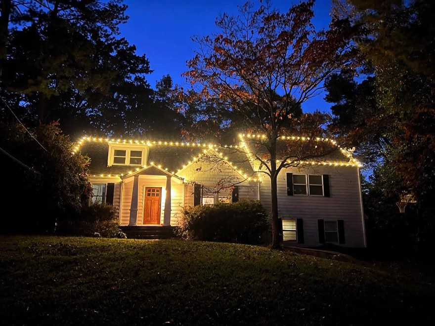 Modest one-and-a-half-story cottage at dusk with a warm-white roofline outline