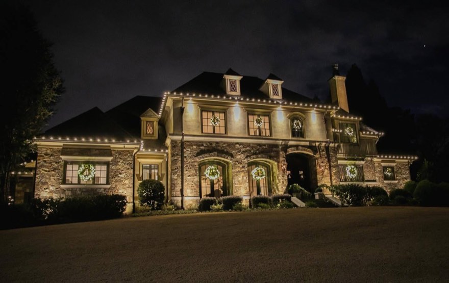 French-country stone manor with the full roofline and dormers outlined and wreaths in every window